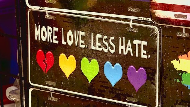 There is a saying at the top: “More Love. Less Hate.” Underneath are five different colored hearts. The first heart is broken.