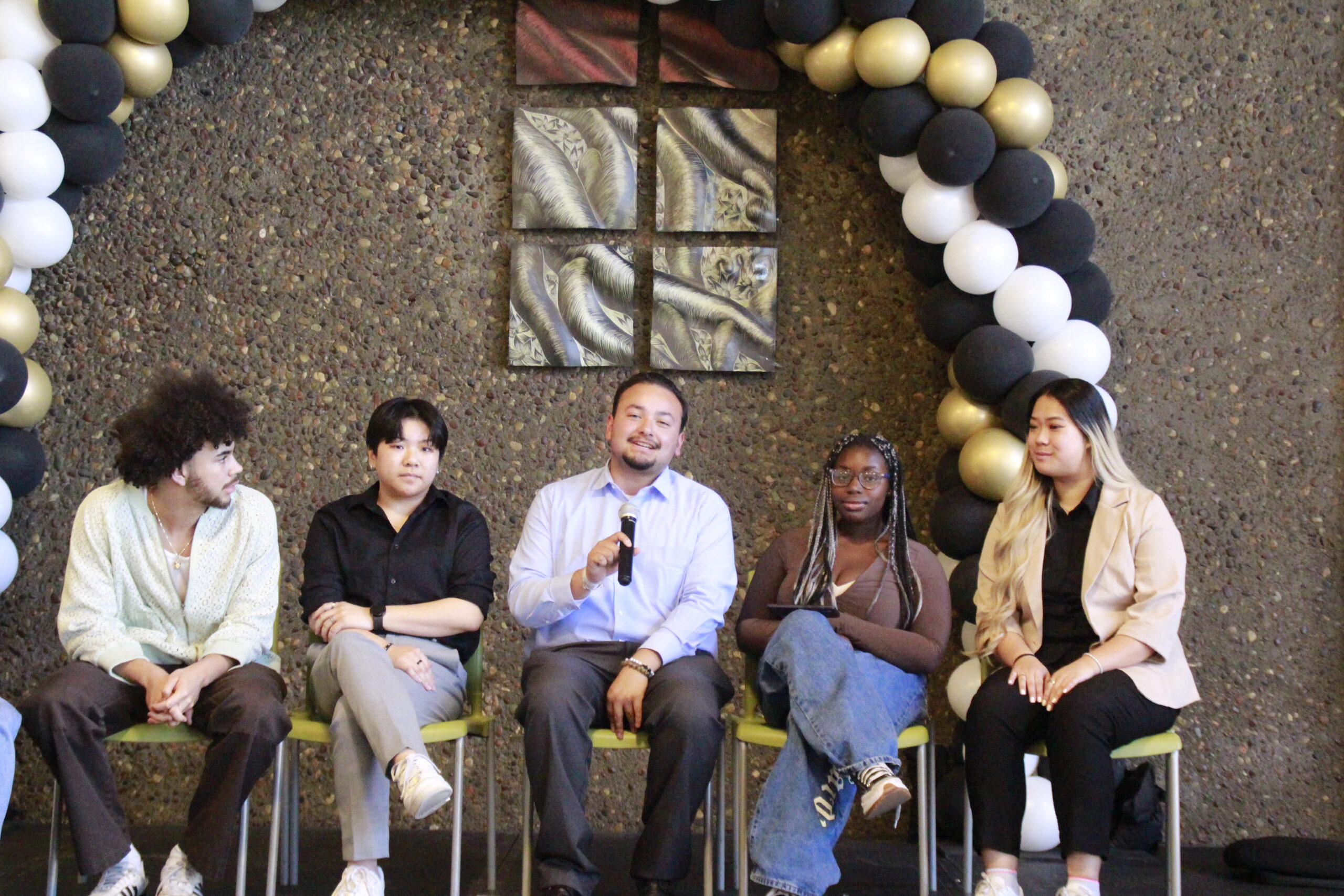 people sitting down in chairs on a stage, holding a microphone answering questions