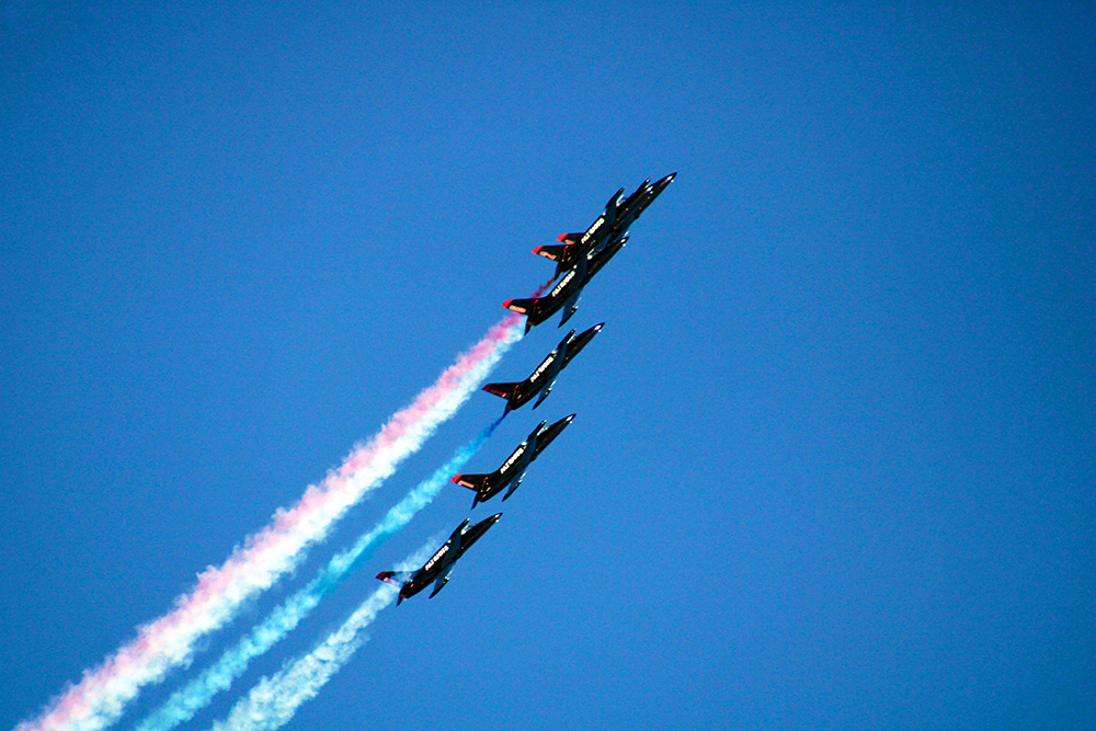 5 jets fly in formation releasing colored smoke