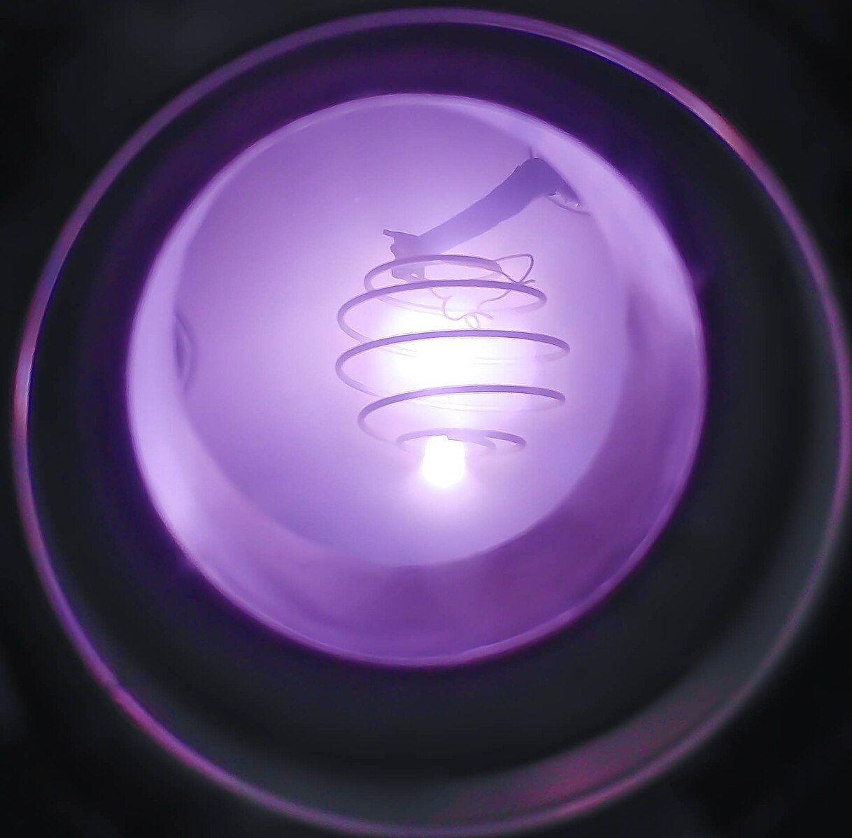 A close-up view inside a fusion reactor chamber showing a glowing purple plasma spiral. The light forms a helical pattern, radiating a soft violet hue within the circular metallic containment vessel.